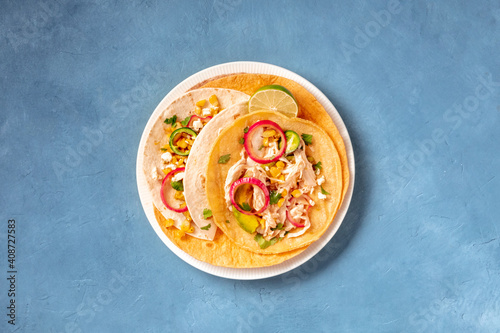 Mexican tacos, tortillas with pulled chicken meat, avocado, sweet corn, and onion, top shot on a blue background