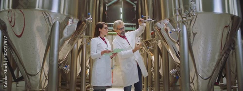 Two scientists in a brewery. Male sceintist pouring beer into a beaker and female scientist taking notes. Factory, brewery concept. photo