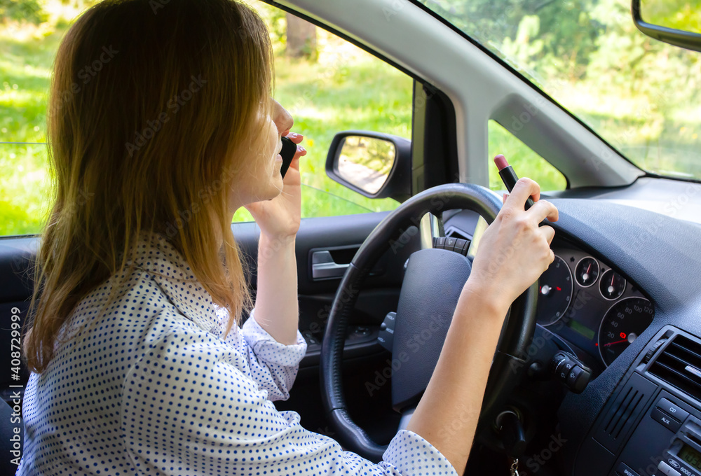Woman is applying makeup in the car. Girl with lipstick behind the wheel talking on the phone. Dangerous situation on the road. Possibility of accident. Woman is applying makeup in the car. Girl with lipstick behind the wheel talking on the phone. Dangerous situation on the road. Possibility of accident.