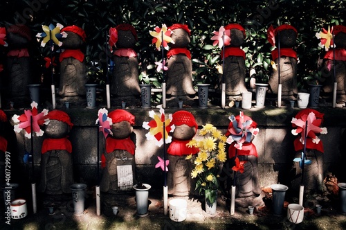 Rows of statues of Jizo Bosatsu decorated with knit caps and bibs and pinwheels to represent deceased children at a cemetery, Tokyo, Japan photo