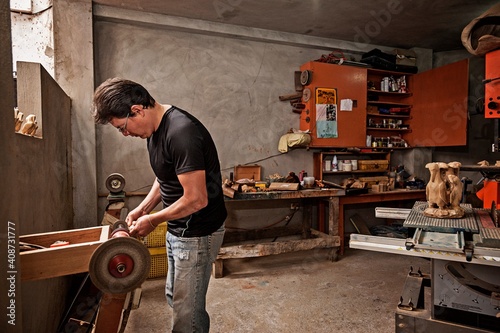 Ecuador, Galapagos Islands, Man using electric wood carving tool to create wood carving sculpture of 1 from
