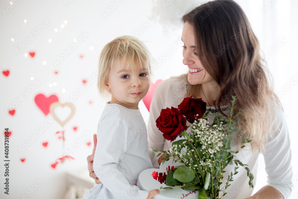 Cute blonde toddler boy, holding box in heart shape and flowers giving them to mom Cute blonde toddler boy, holding box in heart shape and flowers giving them to mom