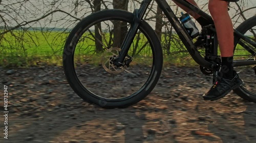 Slow motion of  cyclist pedaling the pedals on the bike. Close-up of a Bicycle wheel driving on gravel. Tracking shot of bike wheel moving.  Men's feet turn the pedals of a mountain bike. Bike tire