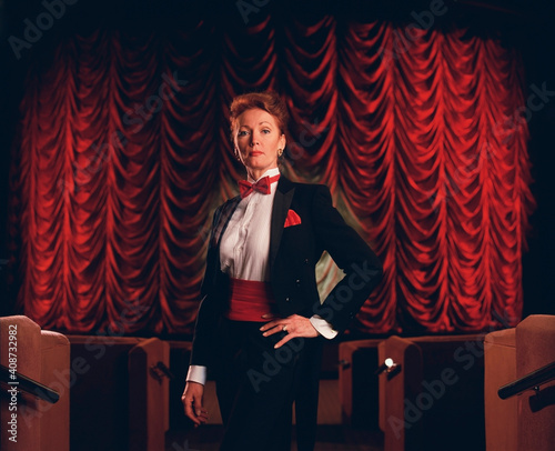 Female usher wearing tuxedo and standing between row of seats in a theater photo
