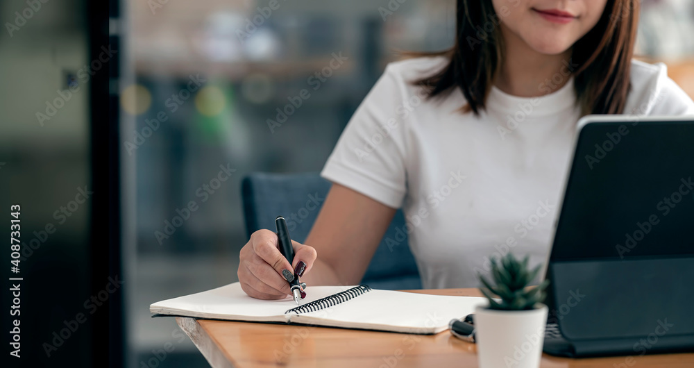 Cropped shot of woman hand using pen writing on notebook while siiting at the table at home Cropped shot of woman hand using pen writing on notebook while siiting at the table at home