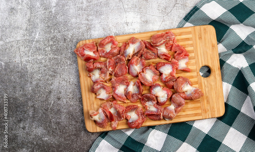 Raw chicken gizzards on a rectangular cutting wooden board on a dark grey background. Top view, flat lay