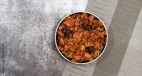 Bigos - traditional polish dish of stewed sauerkraut with prunes and sausages on a round plate on a dark gray background. Top view, flat lay