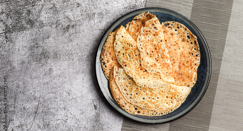 Traditional russian yeast thin pancakes (crepes) on a round plate on a dark gray background. Top view, flat lay