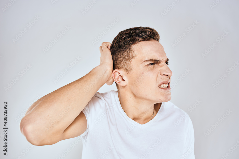 Emotional man in a white t-shirt holds his hand on his face light background Emotional man in a white t-shirt holds his hand on his face light background