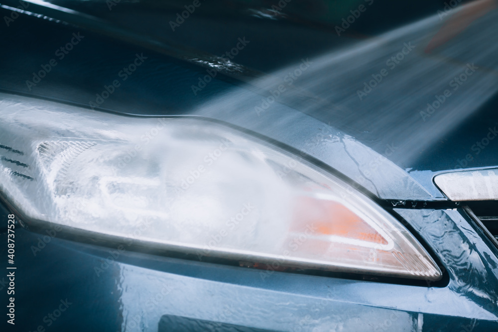 Car wash, headlight cleaning. Car headlight close-up during high pressure water wash