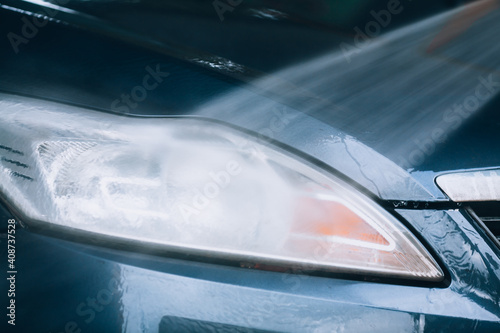 Car wash  headlight cleaning. Car headlight close-up during high pressure water wash