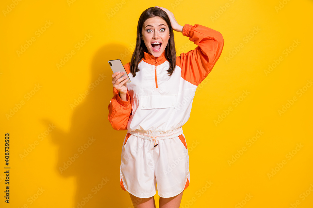 Photo portrait of impressed woman touching head holding phone in one hand isolated on vivid yellow colored background Photo portrait of impressed woman touching head holding phone in one hand isolated on vivid yellow colored background
