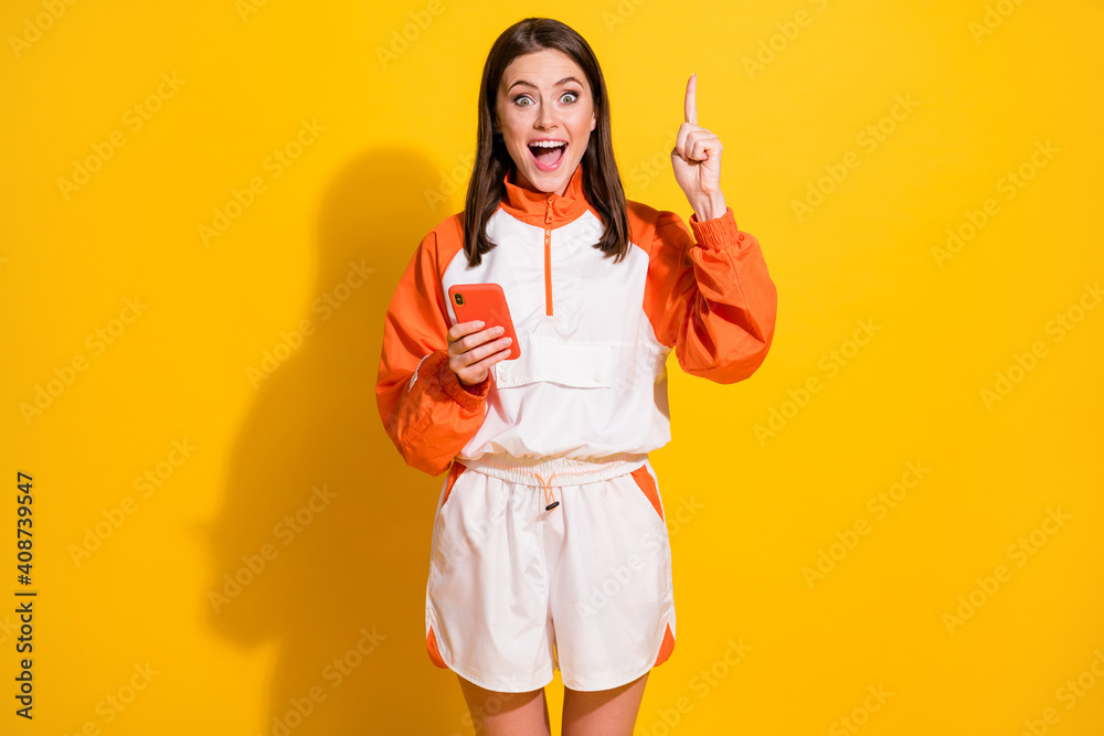 Photo portrait of woman having insight pointing finger up holding phone in one hand isolated on vivid yellow colored background Photo portrait of woman having insight pointing finger up holding phone in one hand isolated on vivid yellow colored background