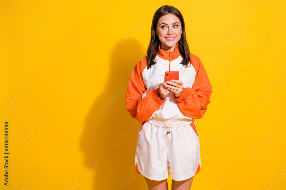 Photo portrait of smiling girl looking at blank space holding phone in two hands isolated on vivid yellow colored background Photo portrait of smiling girl looking at blank space holding phone in two hands isolated on vivid yellow colored background