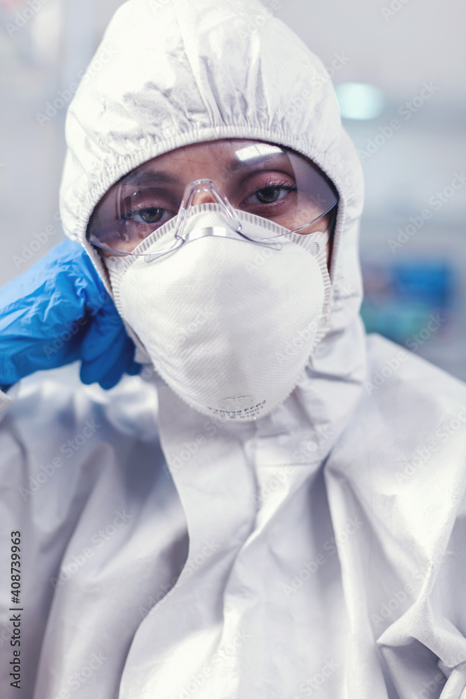 Tired laboratory doctor with overall suit looking at camera in equipped lab. Overworked woman scientist in biotechnology laboratory wearing protective suit during global epidemic. Tired laboratory doctor with overall suit looking at camera in equipped lab. Overworked woman scientist in biotechnology laboratory wearing protective suit during global epidemic.