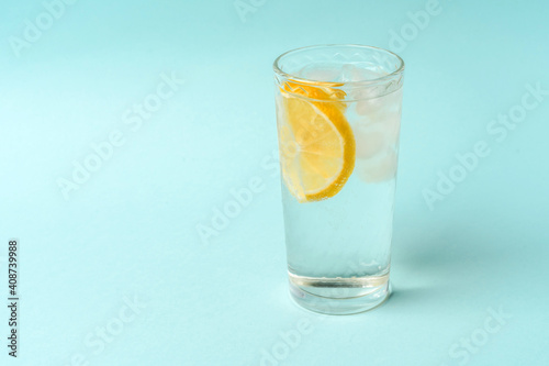 A glass of water with ice and lemon on a light blue background, the concept of a healthy lifestyle