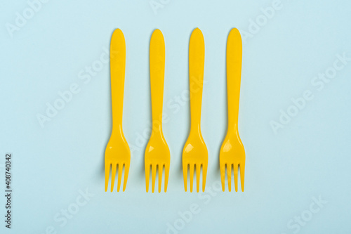 Yellow plastic disposable forks arranged in a row on a blue background, minimalism. The concept of pollution of the environment