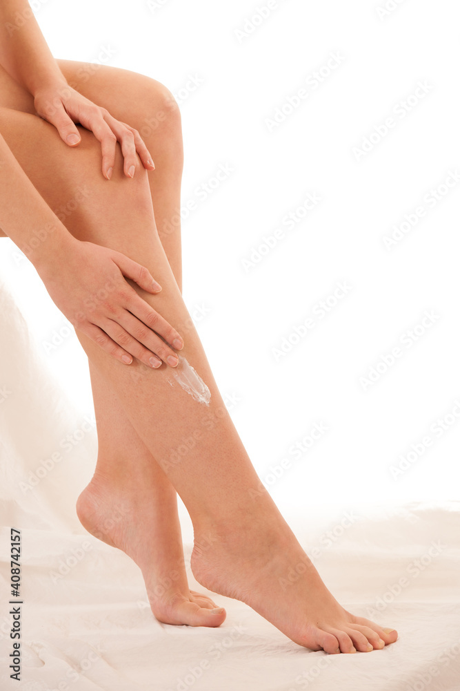Beautiful elegant young woman applying skin cream on her legs isolated over white