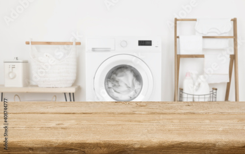 Wooden table in front of washing machine loaded with laundry photo