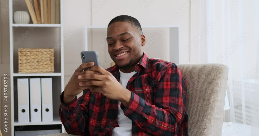 Happy man text messaging using mobile phone on armchair at home