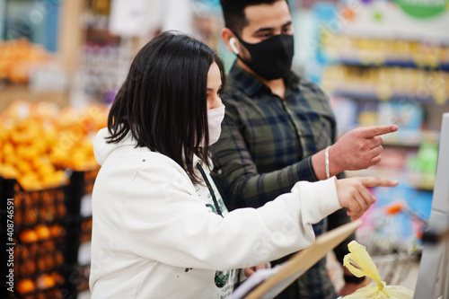Asian couple wear in protective face mask shopping together in supermarket during pandemic. Weigh the goods.