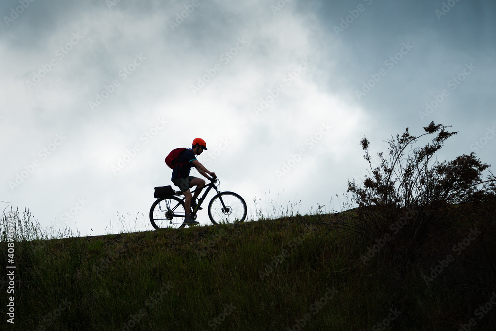 Naklejka premium Silhouette image of a cyclist riding the Otago Central Rail Trail against the cloudy sky, South Island, New Zealand