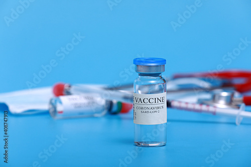 Medical vial with Coronavirus Vaccine COVID-19, , syringe, stethoscope and face mask on blue background with copy space. Vaccination session and immunity improvement.
