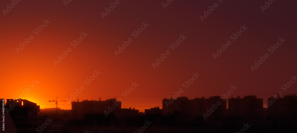 Urban profile with roofs of houses and a construction crane on the background of the sunset sky. Place for your text..Fantastic sunset with bright red sky over the city of Cheboksary, Russia.