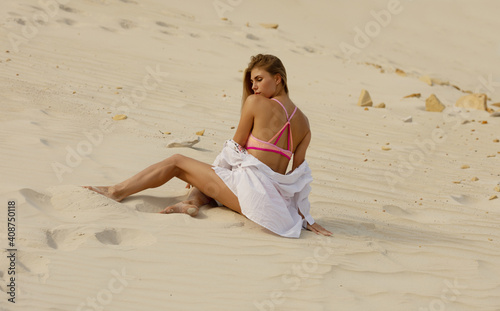 Full length of a sexy female model with blond hair in sexy pink swimsuit on the sand ground in desert.