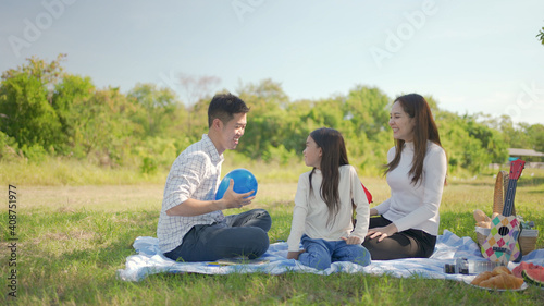 Happy family asian mother and little girl playing balloon and have enjoyed ourselves together during picnicking on a picnic cloth in the green garden. Family enjoying sunny fall day in nature.