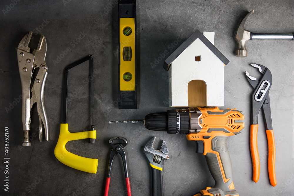 Wooden white house toy and construction tools on Gray-black cement floor background with copy space.Real estate concept, New house.Home repair concept Wooden white house toy and construction tools on Gray-black cement floor background with copy space.Real estate concept, New house.Home repair concept