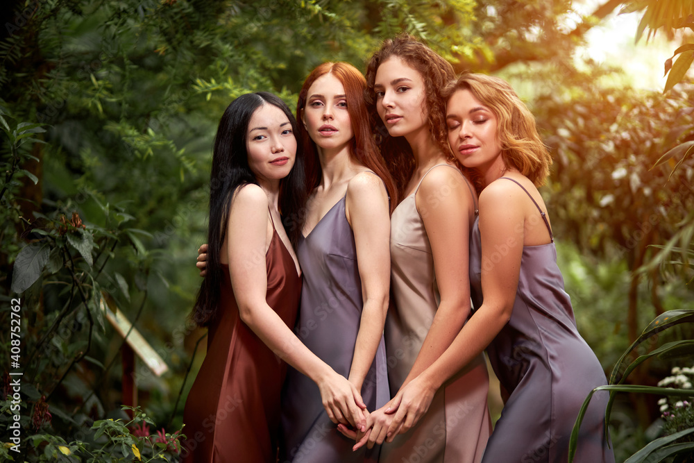 Obraz premium models around green fresh plants, slim slender female in rainforest. women posing at camera wearing silk elegant dress. people and nature