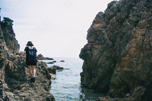 A girl on her back walking on steep rocks by the sea