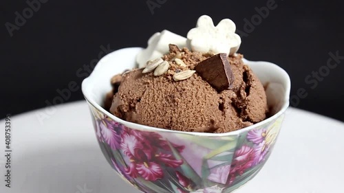 Chocolate ice cream in a bowl, decorated with marshmallows, seeds and chocolate chips. Close-up.