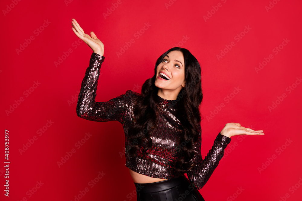 Photo of funny charming girl palms look up empty space wear glossy top isolated red color background Photo of funny charming girl palms look up empty space wear glossy top isolated red color background
