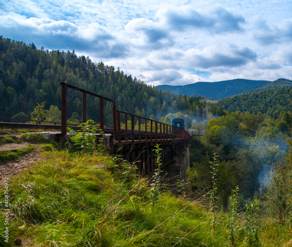 Railway bridge with train train high in the mountains in a beautiful mountainous area, green forest blue sky, mountain landscape, wallpaper, background, postcard