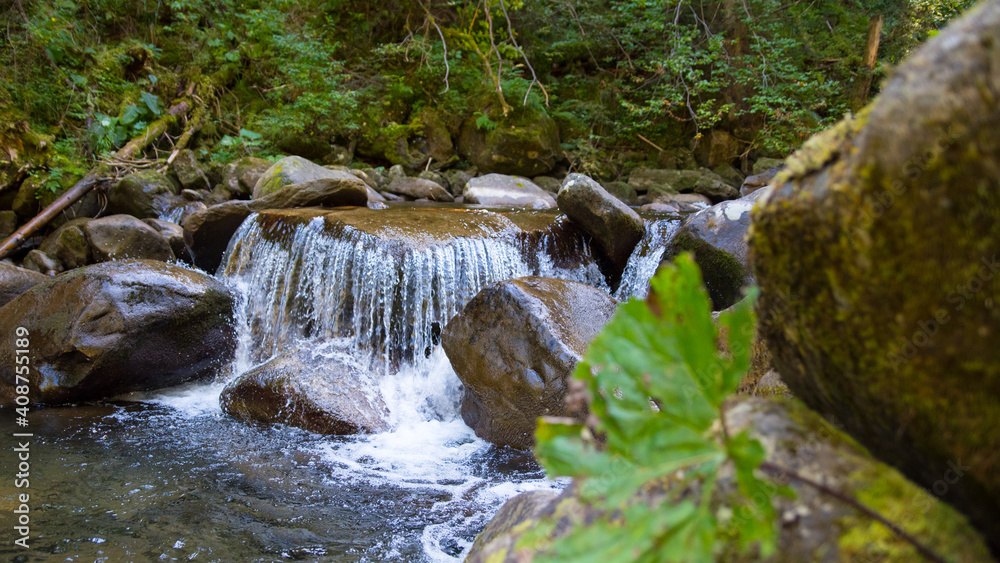 Fototapeta premium Mountain waterfall on a stream in the mountains with a forest, mountain landscape, wallpaper, background, postcard