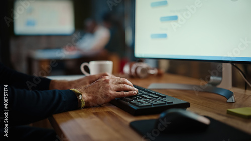 Close Up on Male Hands of a Specialist Working on Desktop Computer in a Busy Creative Office Environment. Manager First Types on a Keyboard and Then Uses the Mouse. He's Wearing a Craft Bracelet.