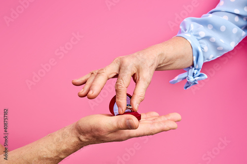 senior couple getting married, man make proposal, give ring in case. woman take ring. isolated pink background