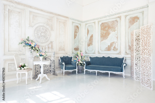 Bright luxury white and blue colored interior living room with flowers in vases. the walls are decorated with baroque ornaments