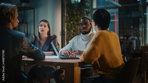 Young Creative Team Meeting with Business Partners in Conference Room Behind Glass Walls in an Agency. Colleagues Sit Behind Conference Table and Discuss Business, App User Interface and Design.