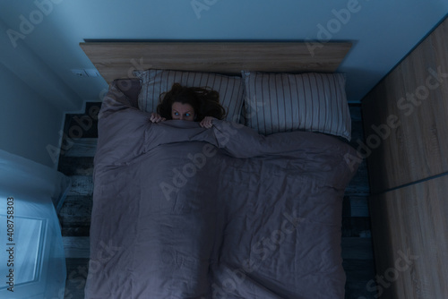 Top view of scared woman alone in bed at night.
