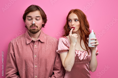 lady in part wear plays with whipped cream, cream on nose of man, isolated on pink background