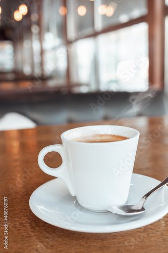 Coffee in a cafe on a wooden table. Drink with steam  smoke. Beautiful blurry background with sideways. Sunlight  interior. Delicious Hot Americano