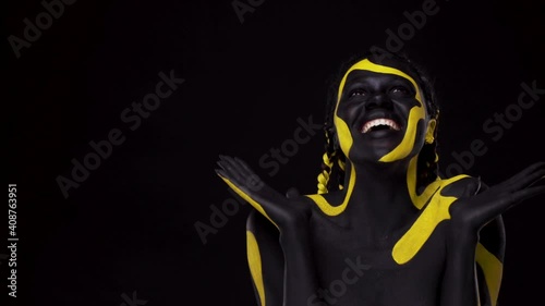 Face art. Woman with black and yellow body paint. Young african girl with colorful bodypaint. An amazing afro american model with yellow makeup. photo