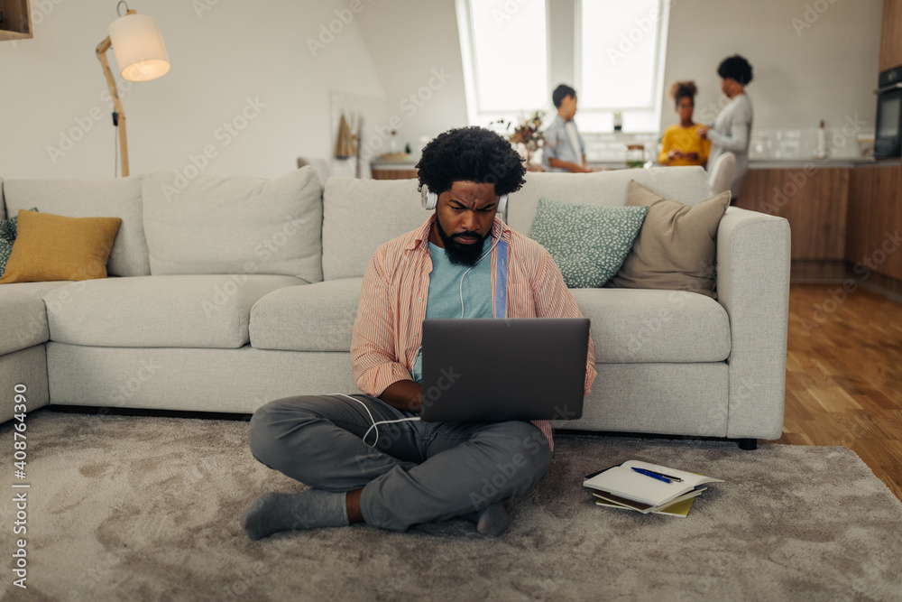 Black man with earphones sitting on the floor and using laptop
