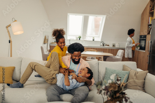 Afro father and his children bonding at home. They are laughing and tickling together photo