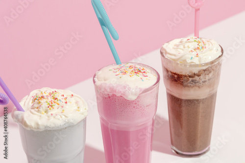 Strawberry, chocolate and vanilla milkshake with whipped cream on pink background. Place for text. Sweet drinks