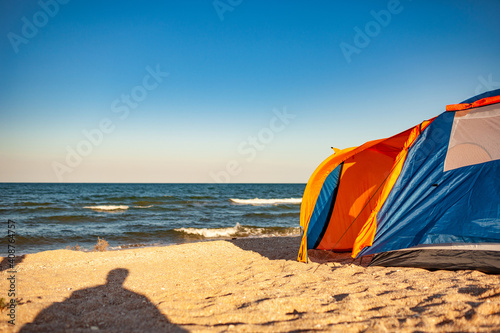 Large comfortable bright tent for rest stands on the shores of the beautiful blue sparkling sea