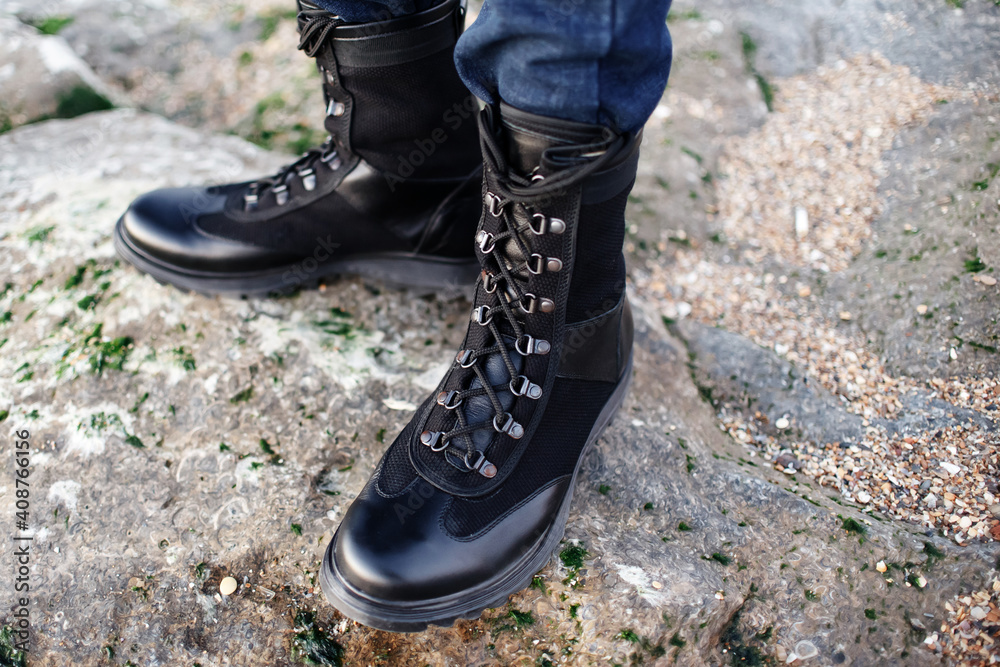 Men's legs in black boots and jeans in the rocky mountains, active holiday excursion